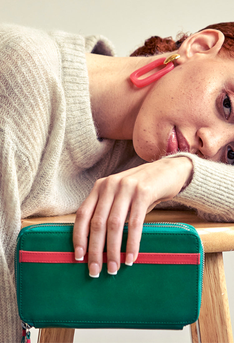 A woman sitting on a stool, holding a green purse.